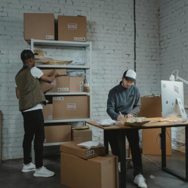 Two workers handling packages and organizing stock in a warehouse setting.